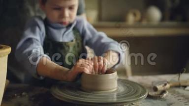 严肃的男孩在儿童中心上陶艺课时，正在用粘土在投掷轮上`花盆。 有意思
